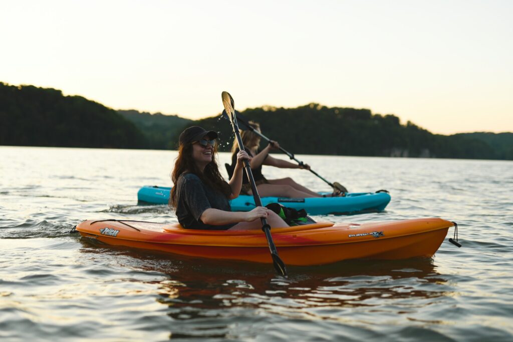 Woman in blue shirt and blue denim jeans riding orange kayak on water during daytime